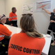 Three traffic controllers are in a room as a Manager is stood up next to a graphic.